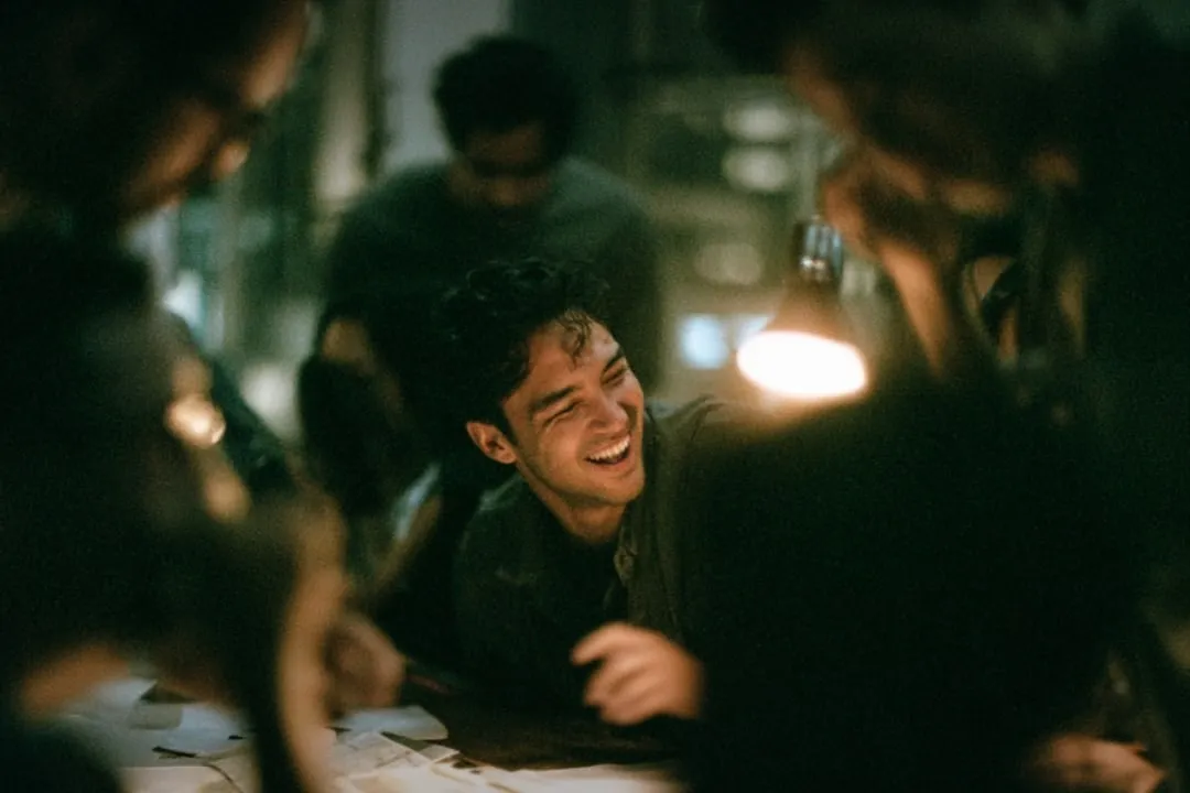 A man laughing across a crowded table, glasses and papers in front of him.