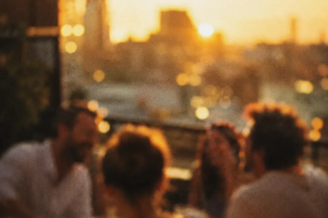 Friends around a rooftop table, the city behind them at sunset.